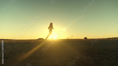 running after sun. training jogging. healthy beautiful girl is engaged in fitness, jogging in country in sun. Jogger girl breathes fresh air on field. Free young woman runs in summer park at sunset.