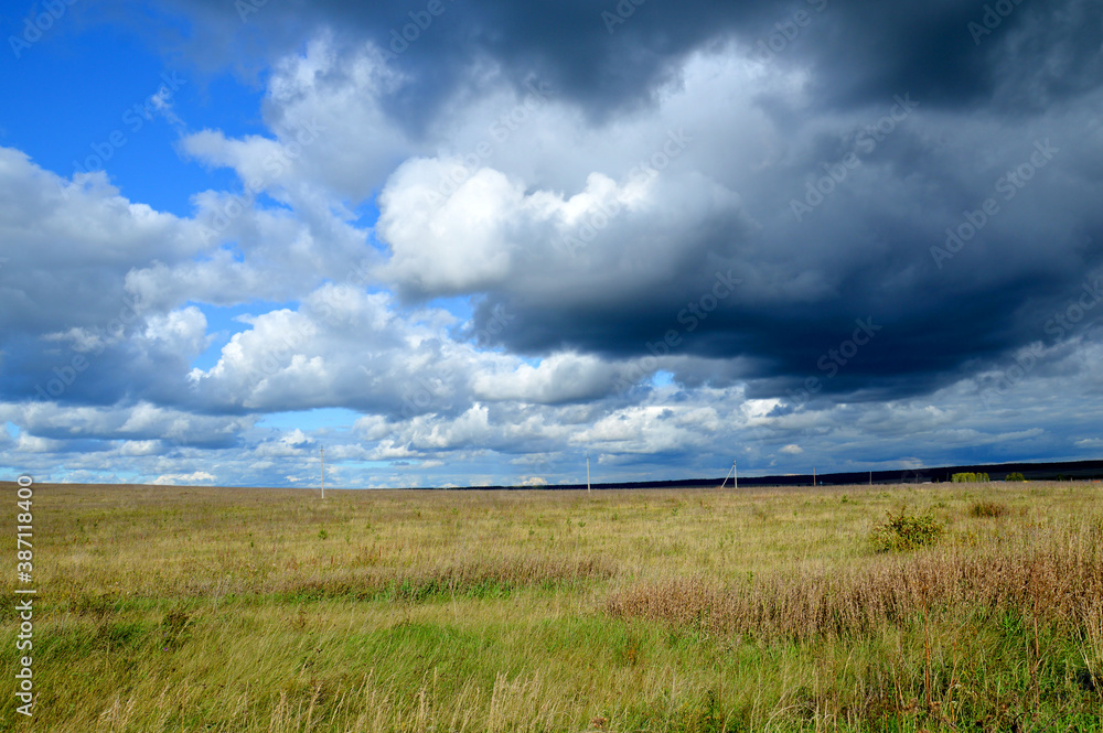 Scenic natural background with field and cloudy sky illuminated by the sun.