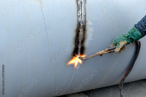 The worker is cutting to metal plate with manual flame cutting process. Oxy-fuel welding, oxyacetylene welding, oxy welding, or gas welding and oxy-fuel cutting are processes that use fuel gases.