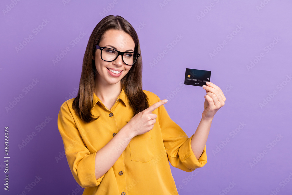 Photo of young pretty lady indicate finger look hold debit card wear spectacles yellow shirt isolated purple color background Photo of young pretty lady indicate finger look hold debit card wear spectacles yellow shirt isolated purple color background