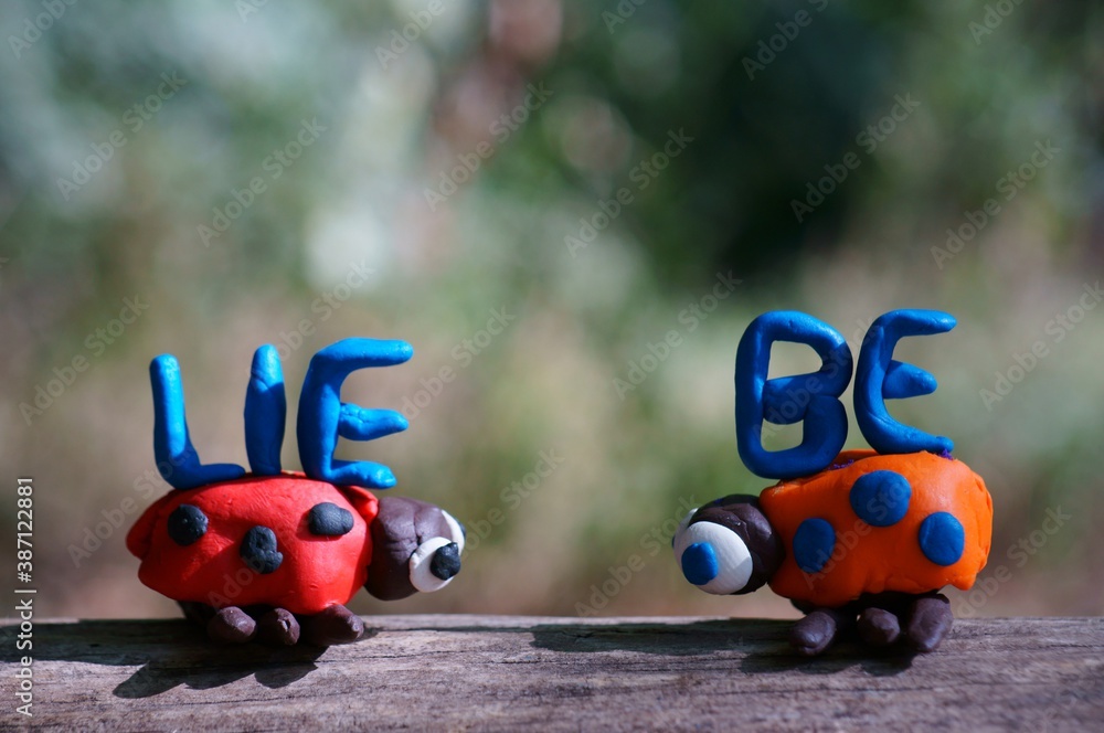 The inscription love in German. Next to it are two figures of ladybirds made of plasticine. The inscription love in German. Next to it are two figures of ladybirds made of plasticine.