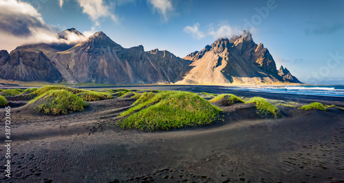 Panoramic summer view of Stokksnes cape with Vestrahorn (Batman Mountain) on background. Splendid morning scene of Atlantic coast with black sand dunes and fresh green grass.