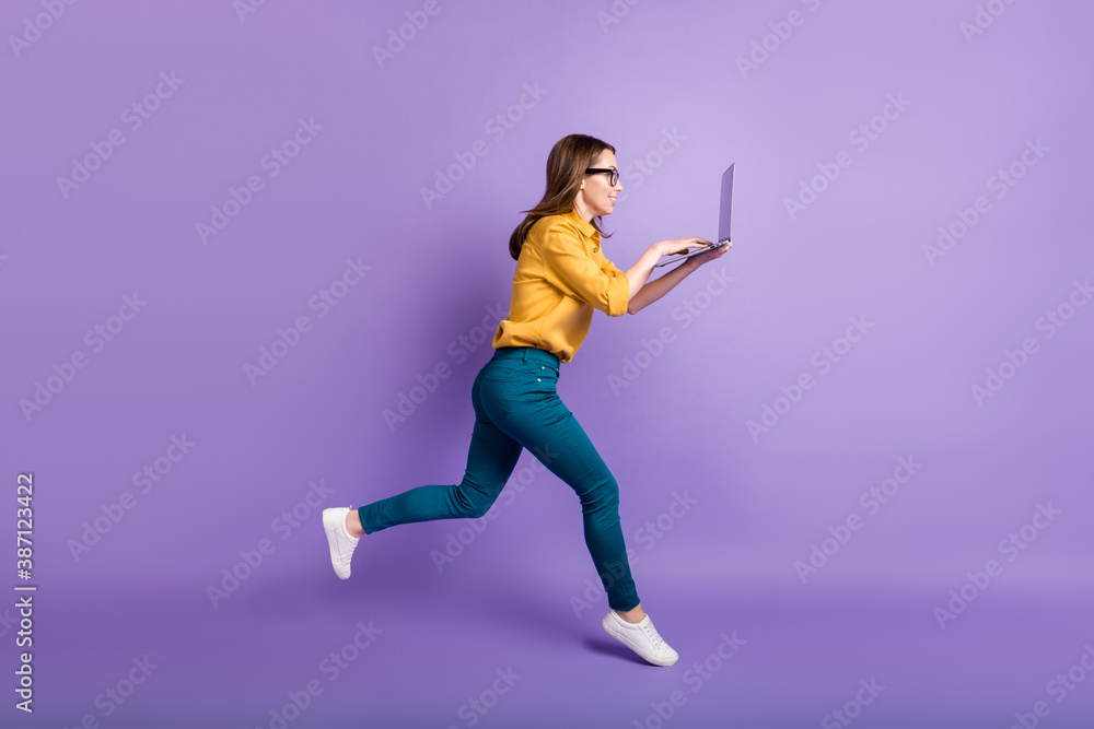 Full length profile photo of girl run hold pc typing touchpad wear yellow shirt blue pants sneakers isolated violet color background