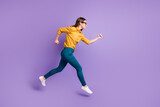 Full length profile photo of girl run jump hurry wear yellow shirt blue trousers sneakers isolated purple color background