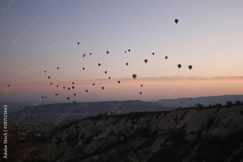Colorful hot air balloons flying over mountains. Aerial view of a beautiful rocky landscape in the evening. Touristic place in Turkey.