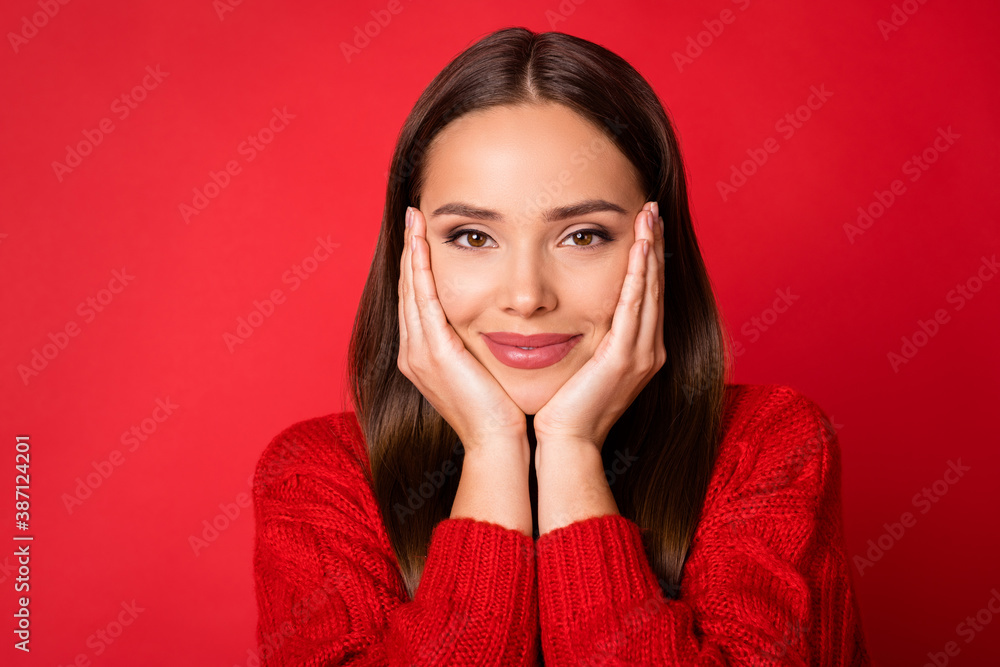 Portrait of lovely girl look in camera with her hands touch cheeks wear sweater isolated over shine red color background Portrait of lovely girl look in camera with her hands touch cheeks wear sweater isolated over shine red color background