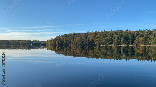 Autumn nature landscape, lake, trees, colorful, foliage, Reflections in calm water. Photography taken in October in Sweden. Blue sky background, copy space and place for text.
