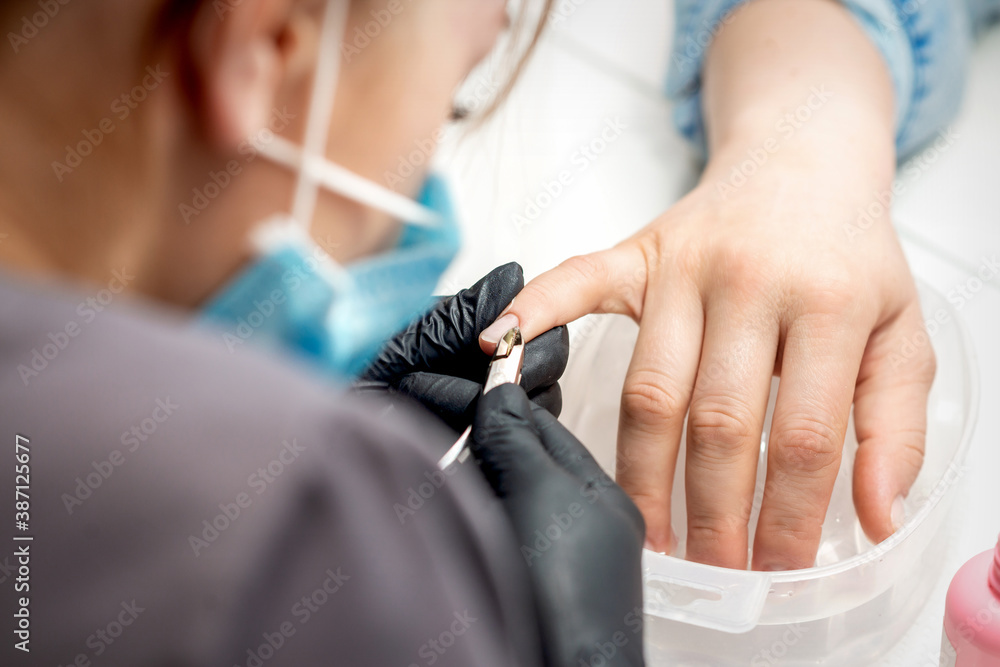 Fototapeta premium Manicure master removes cuticles by professional nail clipper metal tool on female nails in nail salon