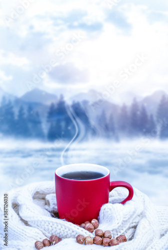 Red cup with coffee, tea on a snowy background, winter forest. A red cup against the background of a winter forest landscape on a soft, cozy scarf. Coffee, tea in the mountains.