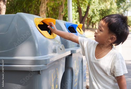 Fotografie Little boy puts a plastic in to the trash in the park