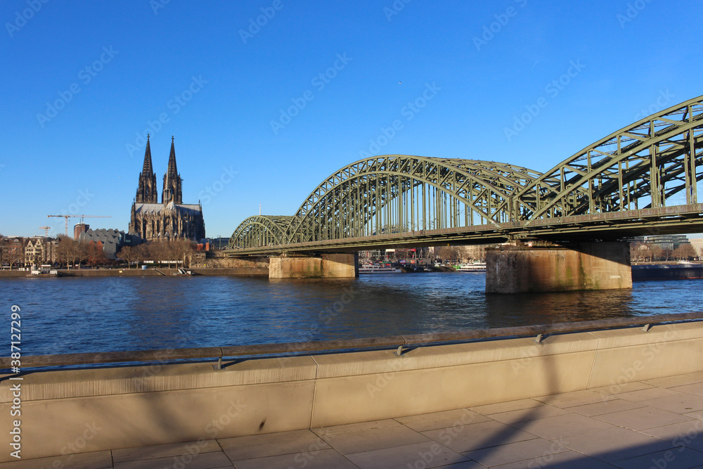 Obraz premium The Hohenzollern bridge over Rhine river on a sunny day. The Cologne Cathedral (Kolner Dom) in the city of Cologne, Germany. It is the largest Gothic church in northern Europe.