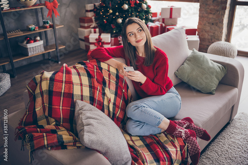 Full size photo of girl sit couch hold smartphone think x-mas holiday plan concept in house indoors with christmas spirit ornament