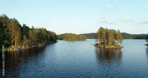 Aerial flight between islands on the lake. Blue water and green trees on warm summer evening. Calm morning water, dawn sky, view from above. Finand.

