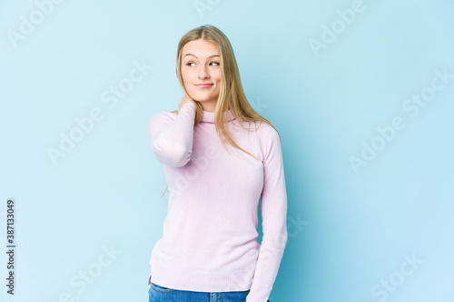 Young blonde woman isolated on blue background touching back of head, thinking and making a choice. © Asier