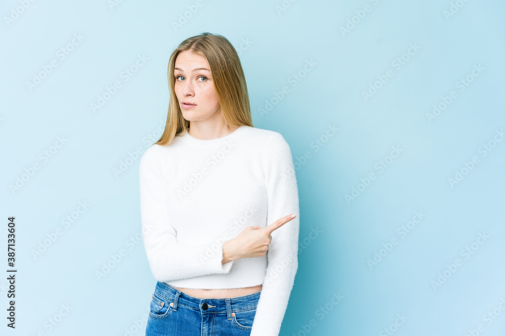 Young blonde woman isolated on blue background smiling and pointing aside, showing something at blank space. Young blonde woman isolated on blue background smiling and pointing aside, showing something at blank space.
