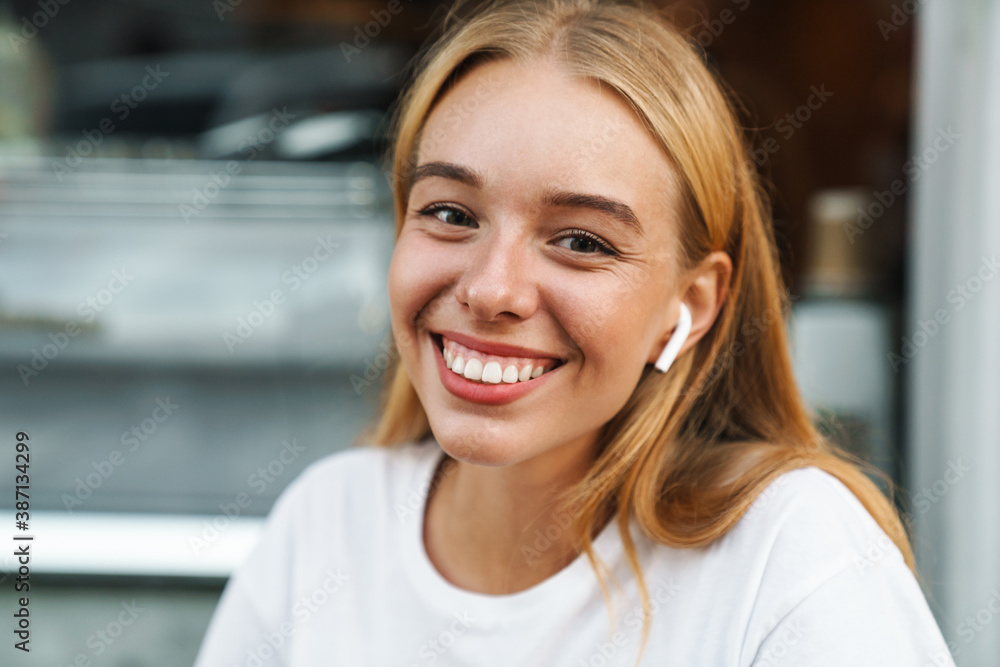 Nice happy girl in earphones looking and smiling at camera outdoors