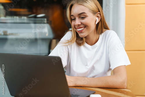 Nice happy blonde girl working with laptop while sitting in cafe