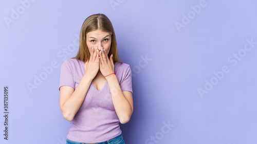 Young blonde woman isolated on purple background shocked covering mouth with hands.