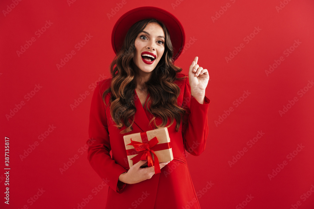 Fototapeta premium Excited beautiful woman pointing finger upward and holding gift box