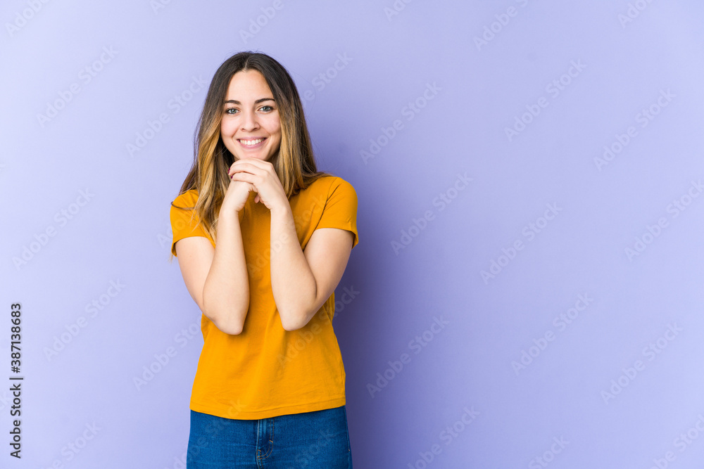 Young caucasian woman isolated on purple background keeps hands under chin, is looking happily aside. Young caucasian woman isolated on purple background keeps hands under chin, is looking happily aside.