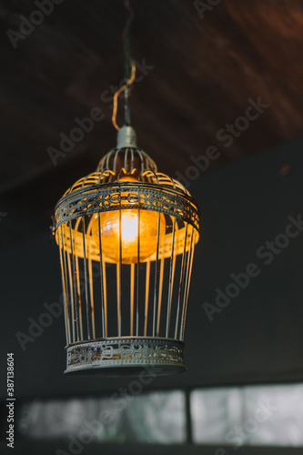 A beautiful metal lamp in the form of a cage with an electric lamp hanging as a decoration on the ceiling close-up. © shchus