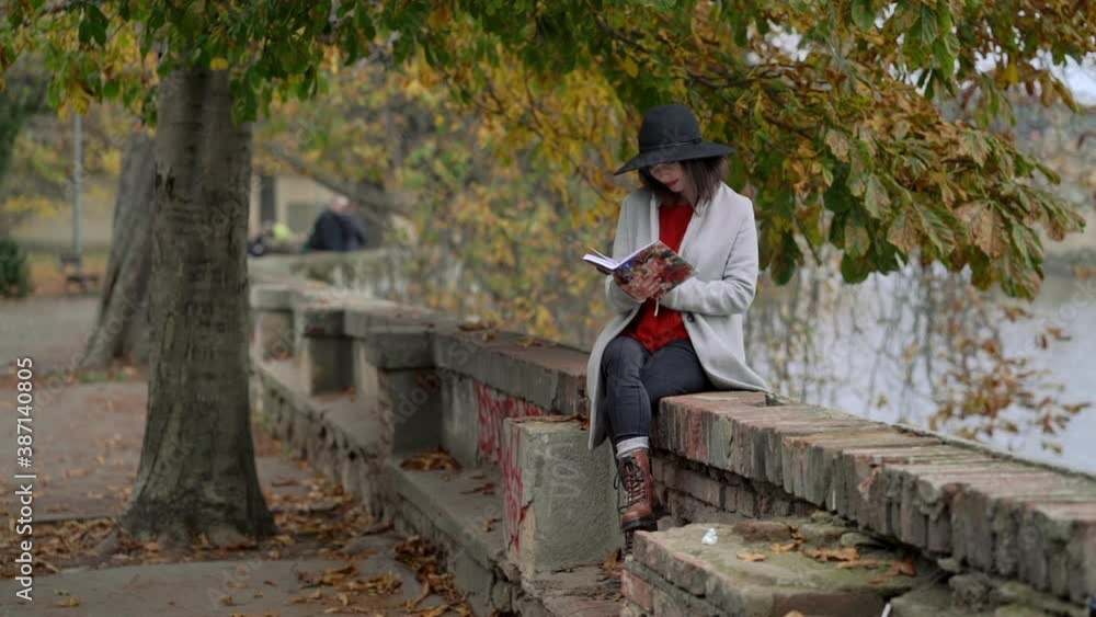Young attractive stylish woman reading book in park by the river at autumn day. Charming cute lady relaxing in park on weekend, studying literature and enjoying loneliness. Young attractive stylish woman reading book in park by the river at autumn day. Charming cute lady relaxing in park on weekend, studying literature and enjoying loneliness.