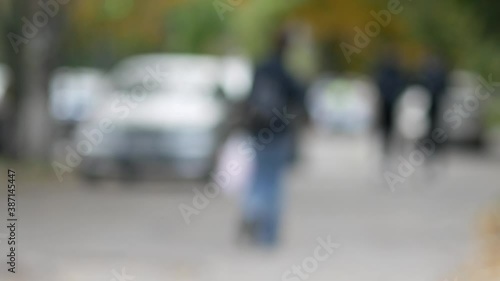 Unrecognizable passers-by are walking down the street. Defocused image. A middle-aged woman with a white plastic bag carries groceries. Backpack. Back view. Autumn day