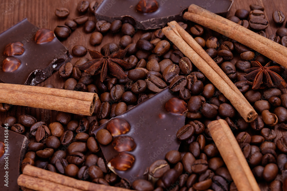 Fototapeta premium Chocolate bar with nuts on a wooden table with coffee beans and spices. Roasted coffee beans, cinnamon sticks and anise stars. Macro shot.