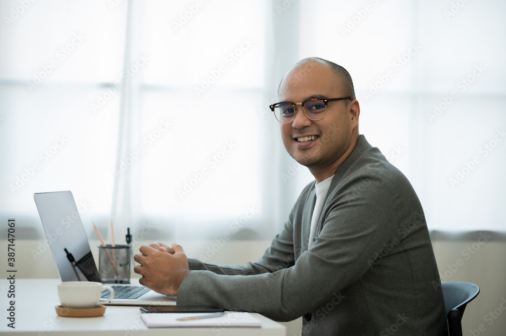 A middle-aged man around the age of 35. Working at home Work through the laptop by meeting video conference. He was wearing a grey suit and glasses. Smiling asian businessman work from home. A middle-aged man around the age of 35. Working at home Work through the laptop by meeting video conference. He was wearing a grey suit and glasses. Smiling asian businessman work from home.
