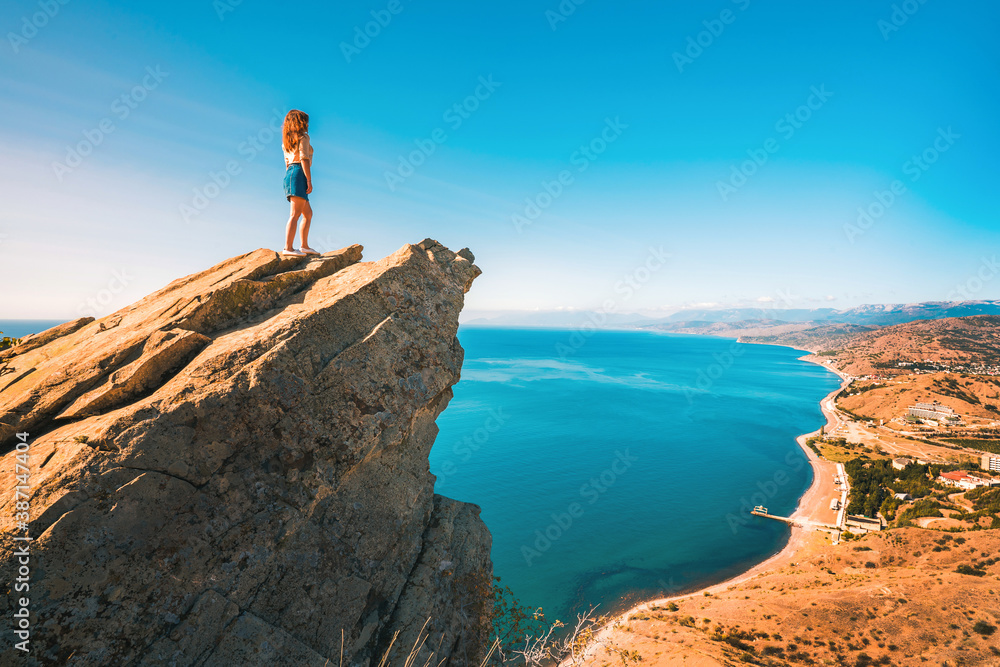 A young woman stands on a picturesque rock ledge above the sea against the sky. The concept of travel and freedom. 