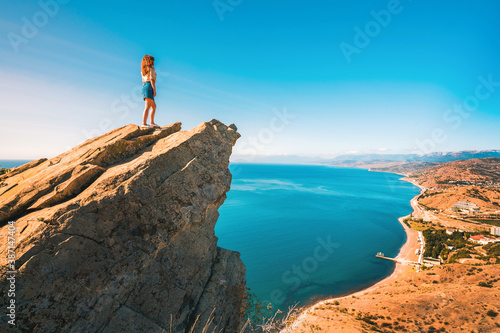 A young woman stands on a picturesque rock ledge above the sea against the sky. The concept of travel and freedom.  © KseniaJoyg