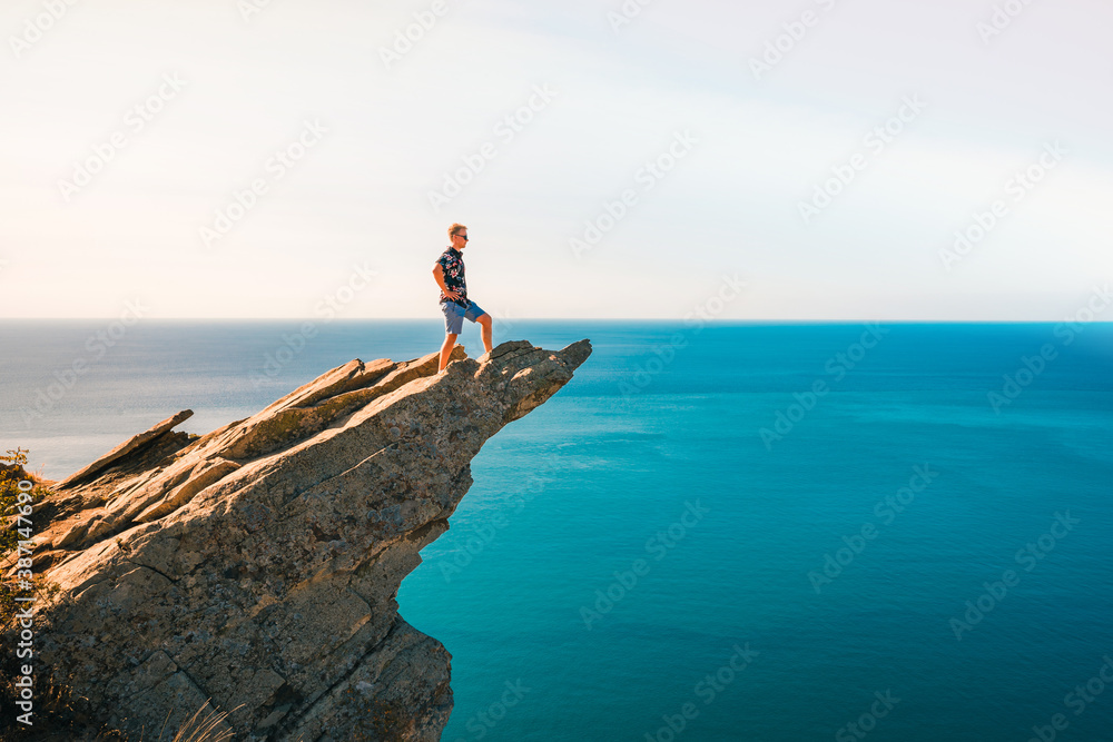 A young man stands on a picturesque rock ledge above the sea against the sky. The concept of travel and freedom. 
