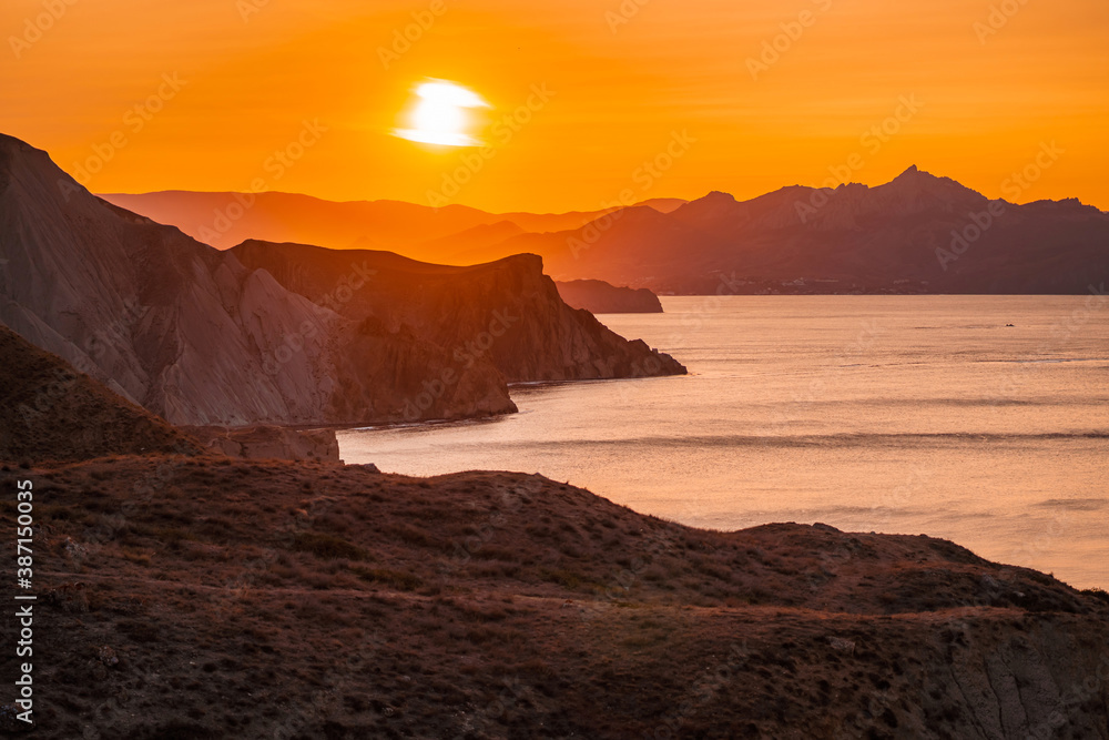Hilly landscape by the sea in a bright orange sunset. Layers of mountains at sunset, background image Hilly landscape by the sea in a bright orange sunset. Layers of mountains at sunset, background image