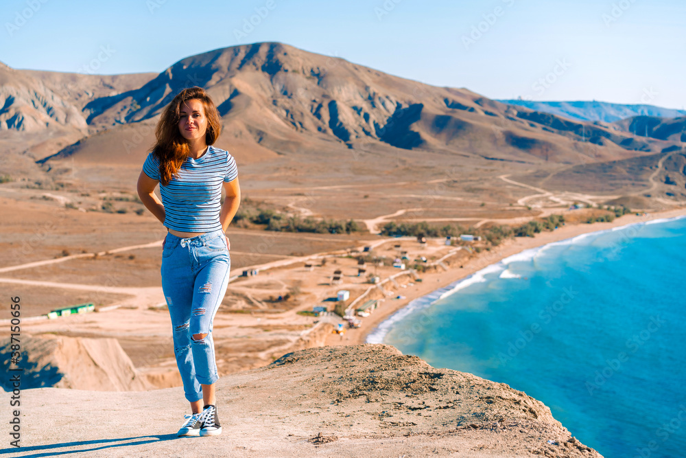 A young woman with long hair stands on the slope of Cape chameleon with an amazing panoramic view of the hills and the sea from above