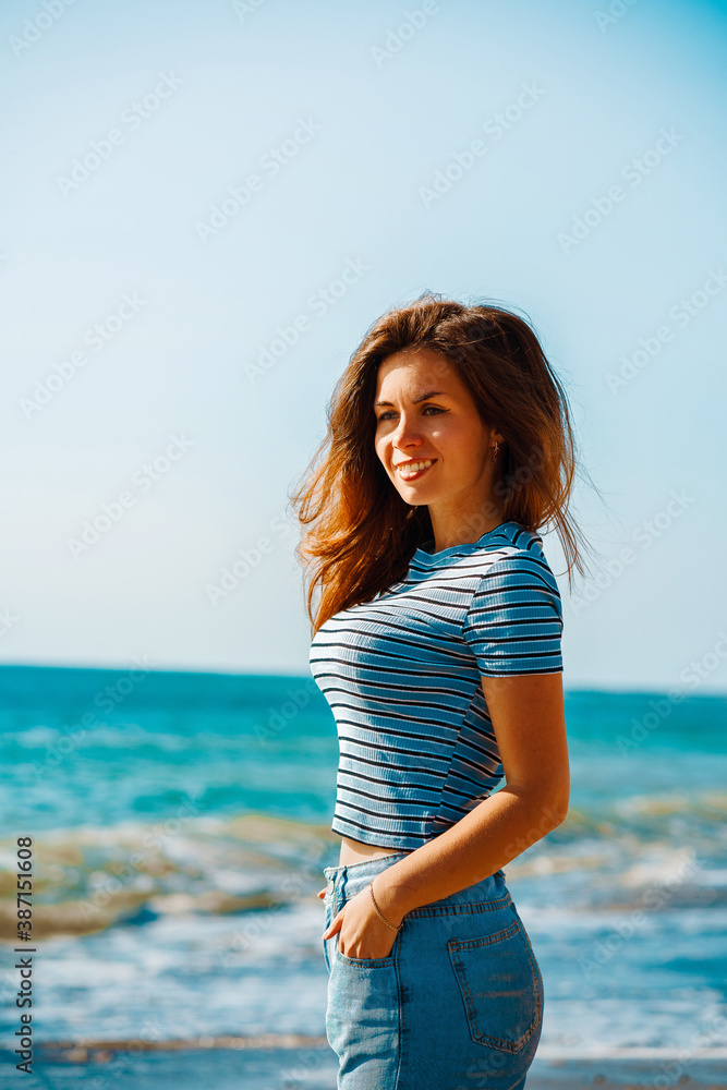 A beautiful young brunette woman in jeans walks along a picturesque sandy beach A beautiful young brunette woman in jeans walks along a picturesque sandy beach