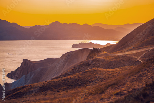 Hilly landscape by the sea in a bright orange sunset. Layers of mountains at sunset, background image © KseniaJoyg
