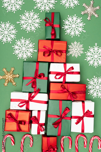 top view of multicolored gift boxes with red ribbons  and decorative snowflakes on green background