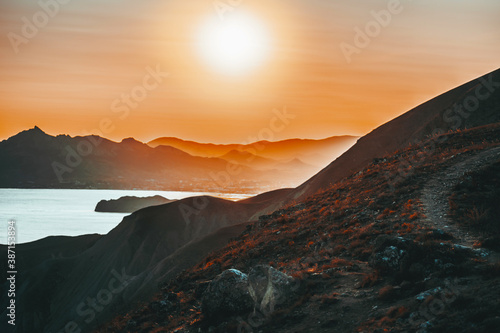 Hilly landscape by the sea in a bright orange sunset. Layers of mountains at sunset, background image