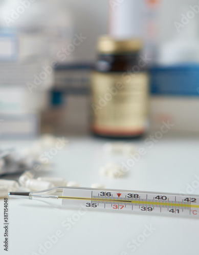 Bottle pills and medicine capsule on table, drugs and tablets boxes in background. Medical thermometer with a temperature of 38 degrees. Increased body temperature of a sick person. 