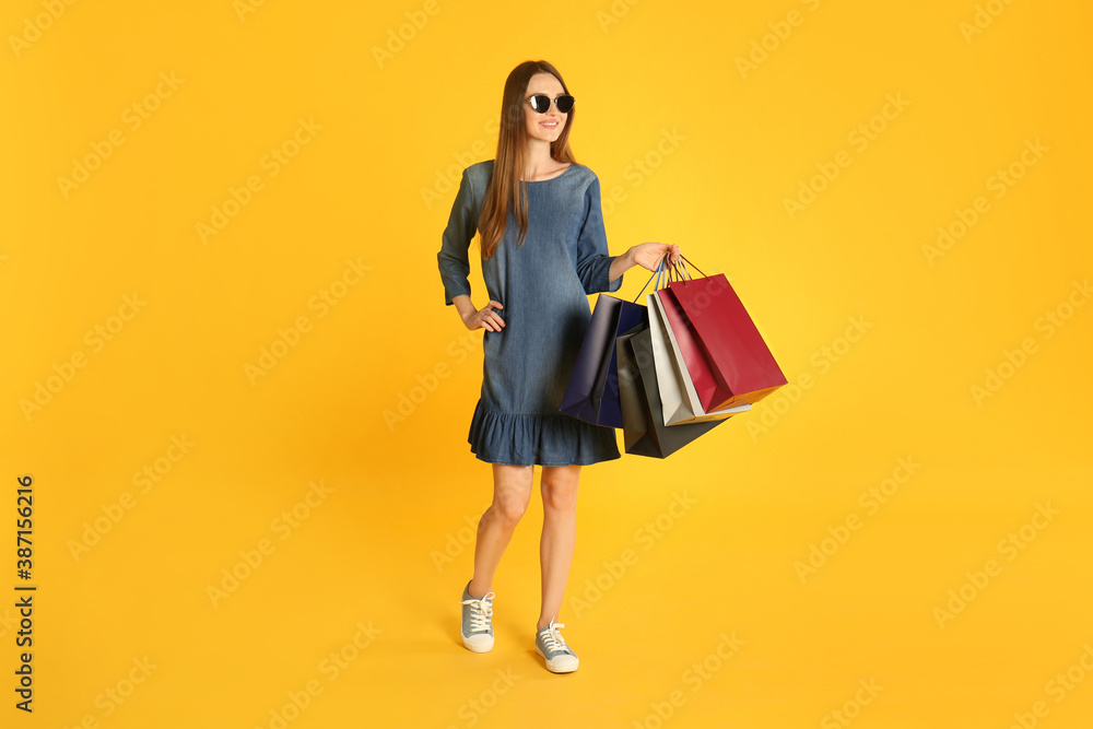 Beautiful young woman with paper shopping bags on yellow background Beautiful young woman with paper shopping bags on yellow background