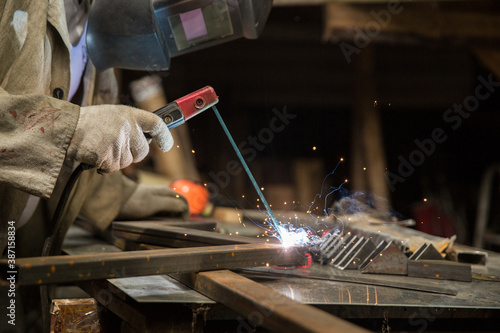 Photos welder welds a metal structure in a workshop with electrical welding