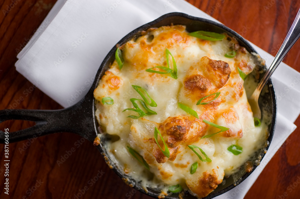 Potatoes au gratin. Potatoes baked in butter, cheese cream sauce, garnished with scallions, parsley and served in cast iron skillet. Classic American restaurant or French bistro side dish. Potatoes au gratin. Potatoes baked in butter, cheese cream sauce, garnished with scallions, parsley and served in cast iron skillet. Classic American restaurant or French bistro side dish.