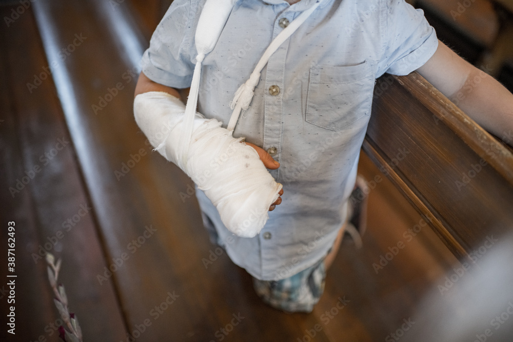 A kid with broken arm and cast on it. Young boy in pain standing. A kid with broken arm and cast on it. Young boy in pain standing.