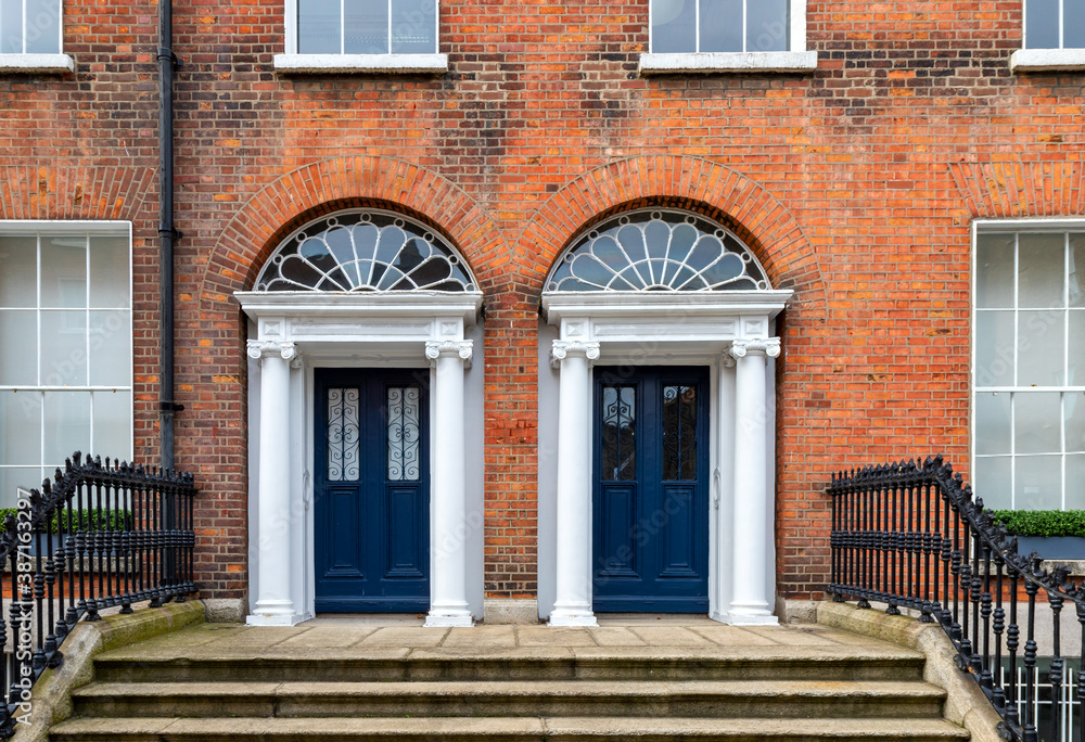 Two blue paneled Georgian doors, with glass insets and matching decorative lead fanlights, stone columns, granite steps and iron railings. Dublin, Ireland. Exterior front of red brick buildings