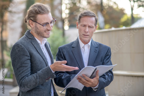 Two male collegaues checking papers outside, discussing business issues photo