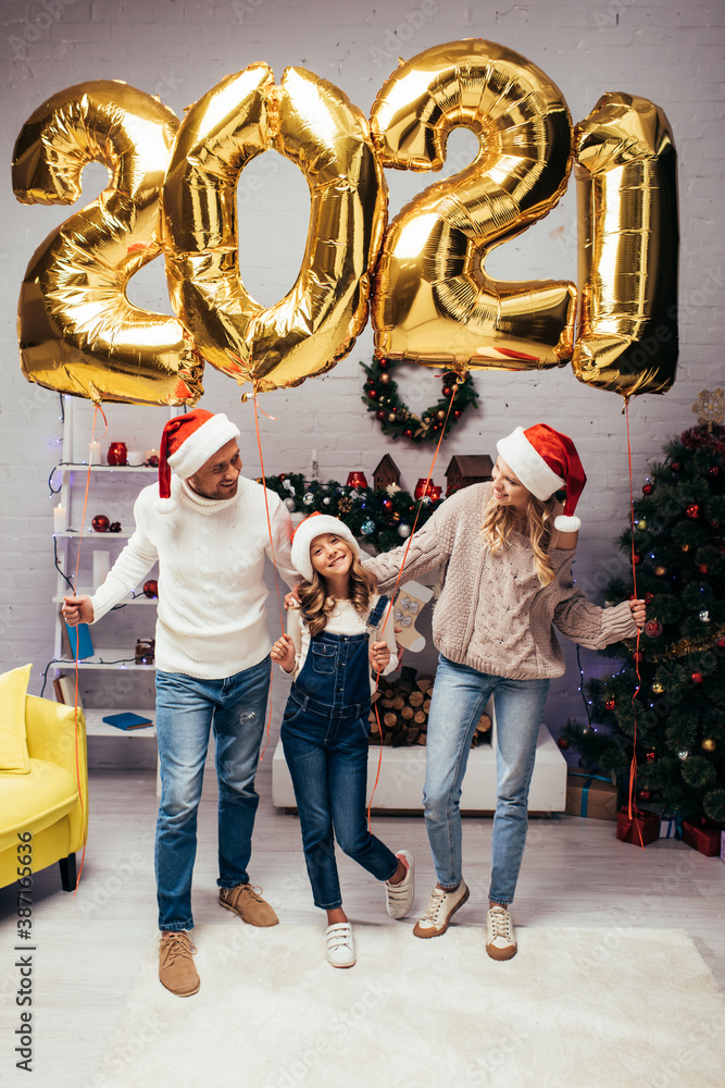 happy family in santa hats standing near presents and shiny balloons with 2021 numbers