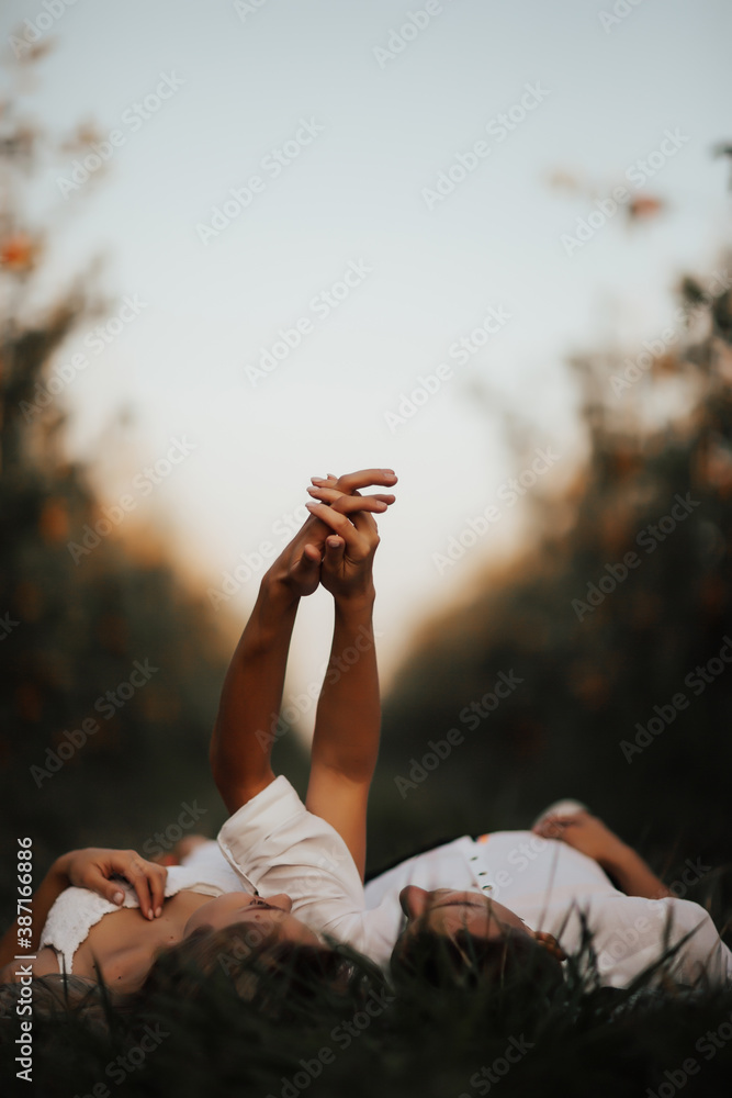 Young couple lying on green lawn while spending time together in park. Romantic atmosphere. They holding hands.  - obrazy, fototapety, plakaty 