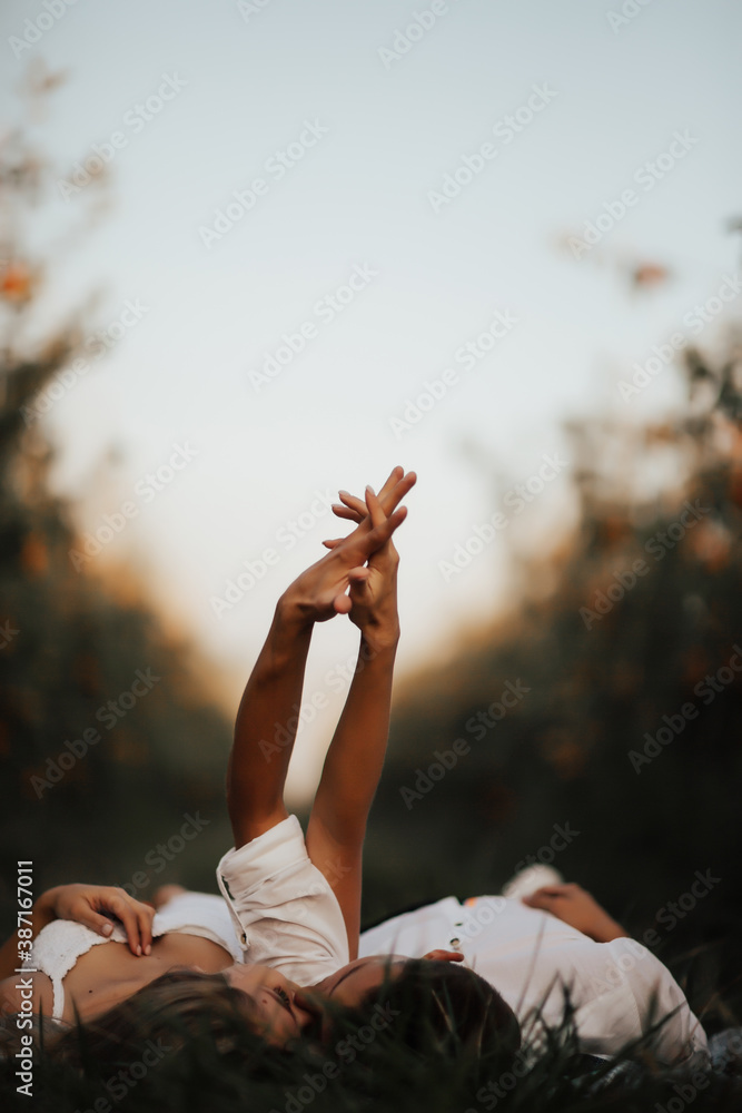 Relaxed young couple lying on green lawn, are kissing with closed eyes and holding hands.