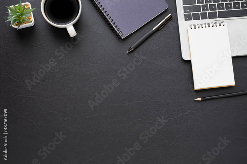 Top view above of Black leather office desk table with keyboard  notebook and coffee cup with equipment other office supplies. Business and finance concept. Workplace  Flat lay with blank copy space.