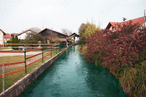 Small river goes in village between houses, autumn season time. Deep water. photo